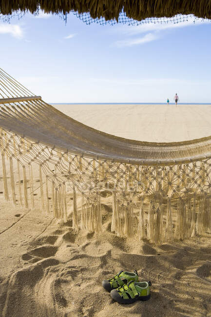 Hamac sur la plage, empreintes de pas et une paire de baskets sur le sable blanc — Photo de stock