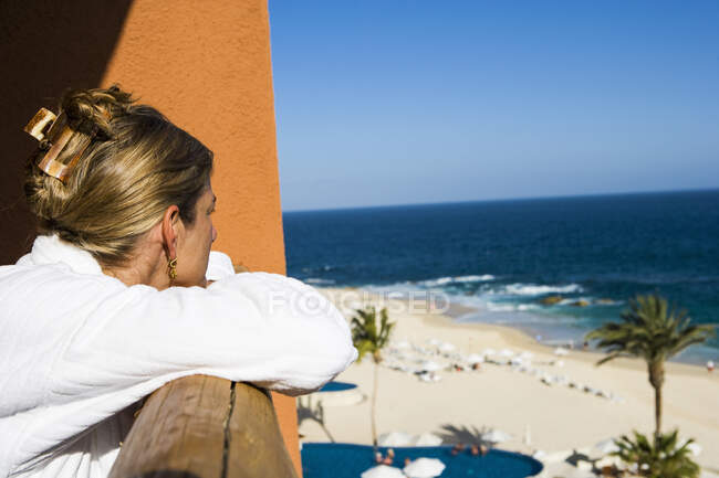 Доросла жінка на балконі готелю з видом на спокійний блакитний океан і білий піщаний пляж — стокове фото