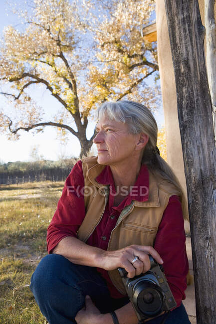 Mature woman at home on her property in a rural setting, holding a camera — Stock Photo