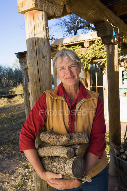 Зрелая женщина дома на своей территории в сельской местности с бревенчатыми бревнами — стоковое фото