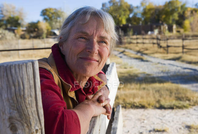 Mature woman at home on her property leaning on a gate. — Stock Photo
