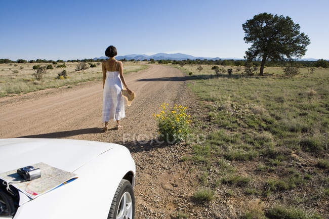 Mujer nativa americana en vestido de sol conduciendo un coche deportivo convertible blanco en tierra del desierto - foto de stock