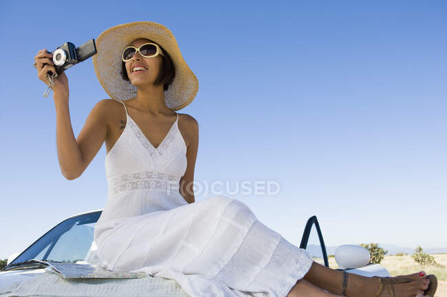 Mujer nativa americana en vestido de sol sentado en un coche deportivo convertible blanco, tomando fotos - foto de stock