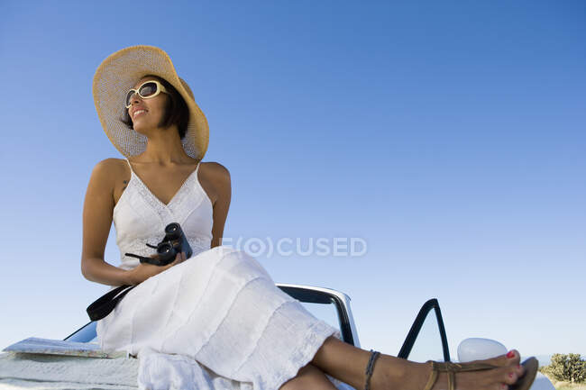 Корінна американська жінка в сонцезахисному одязі сидить на білій кабріолет спортивній машині. — стокове фото