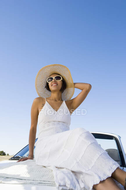 Mujer americana nativa en vestido de sol sentado en coche deportivo convertible blanco - foto de stock