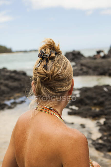 Вид ззаду жінки на пляжі, що виглядає над камінням — стокове фото