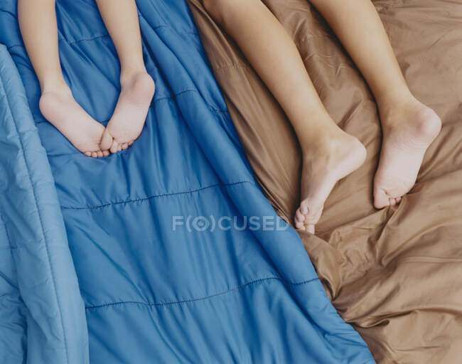 Due fratelli sdraiati su sacchi a pelo in tenda, gambe nude e piedi nudi. — Foto stock