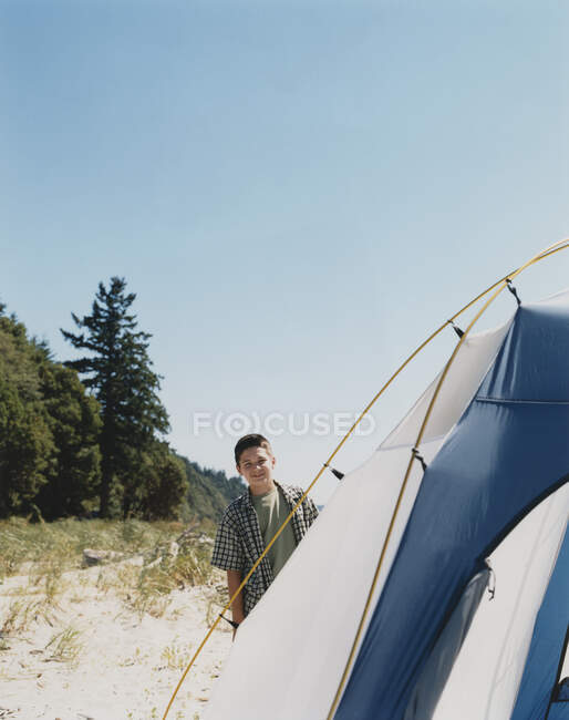 Jovem de pé fora da barraca de acampamento na praia — Fotografia de Stock