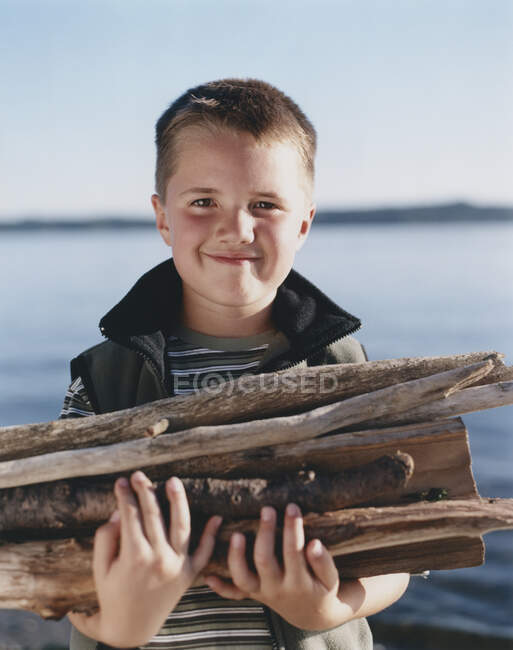 Portrait of happy young boy holding pile of firewood, — Stock Photo