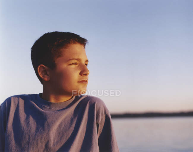 Garçon regardant au loin sur une plage au coucher du soleil — Photo de stock