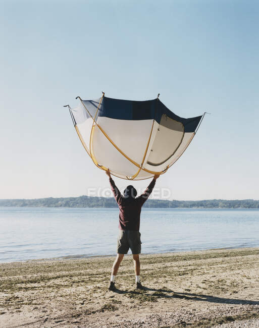 Uomo che tiene una piccola tenda a cupola sopra la testa, in piedi sulla spiaggia — Foto stock