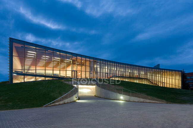 Modernos edificios universitarios, fachada de cristal iluminada por la noche, sobre una superficie curva - foto de stock