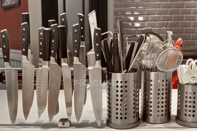 Gewerbliche Arbeitsplatte in der Küche, Messerreihen auf einem Magnetstreifen und Utensilien in Töpfen. — Stockfoto