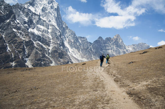 Dos escaladores en un sendero frente a las empinadas montañas. - foto de stock
