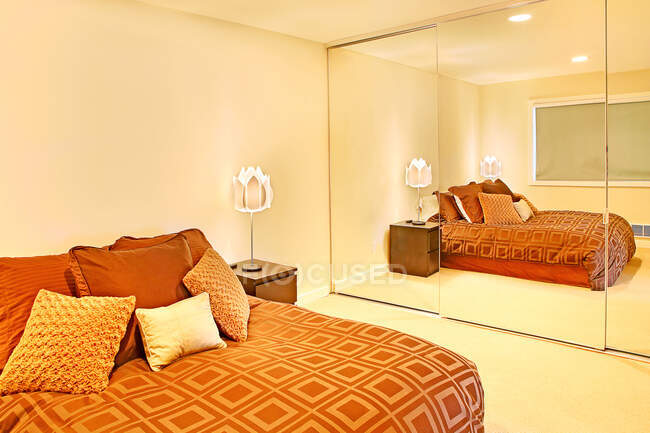 Une chambre avec un grand lit double et une literie colorée, et des placards au plafond et au sol. — Photo de stock