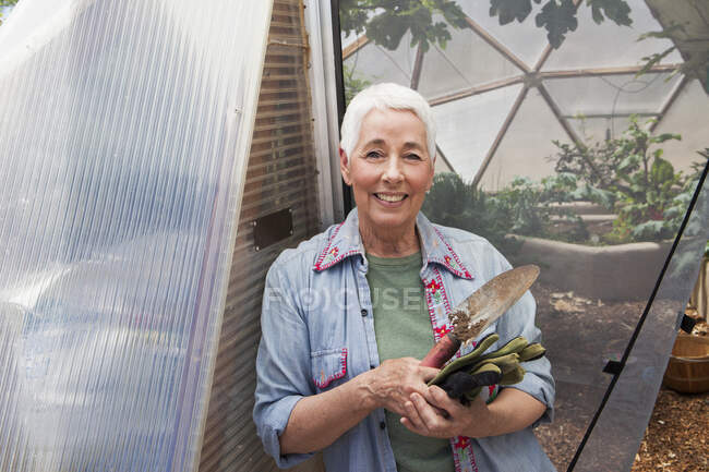 Jardinería de mujer mayor sonriente en una cúpula geodésica, casa de vidrio climatizada - foto de stock