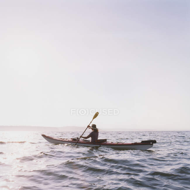 Donna di mezza età kayak da mare al tramonto, vista laterale — Foto stock