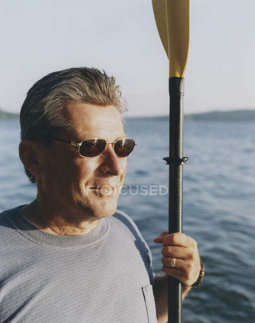 Retrato de homem de meia idade segurando mar caiaque remo ao entardecer — Fotografia de Stock