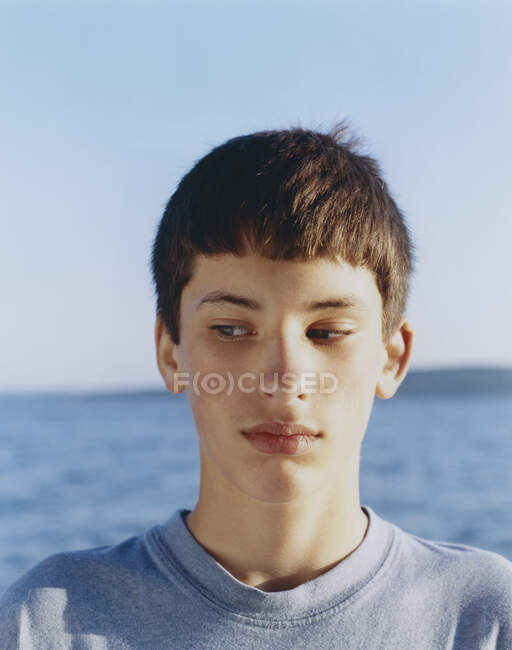 Portrait  of serious adolescent boy looking away, ocean in distance — Stock Photo