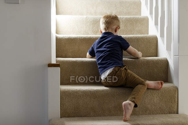 Um menino sentado nas escadas em casa, vista para trás. — Fotografia de Stock