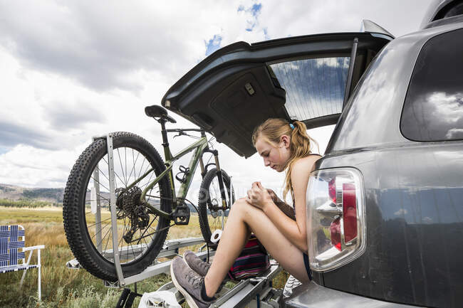 Adolescente sentada na bagageira de um SUV olhando para a vista — Fotografia de Stock