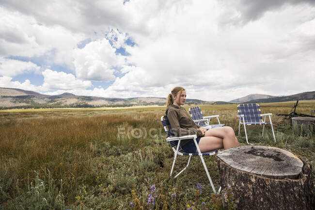 Adolescente chica sentada en silla plegable en un paisaje abierto - foto de stock