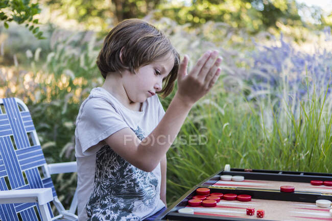 Um menino jogando gamão ao ar livre em um jardim. — Fotografia de Stock