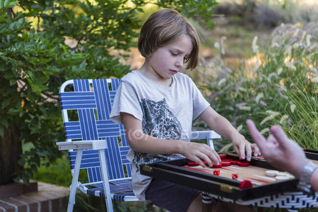 Un ragazzo che gioca a backgammon all'aperto in un giardino. — Foto stock