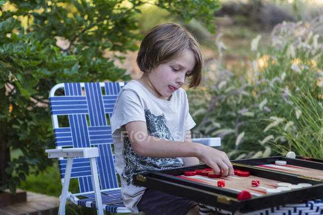Un jeune garçon jouant au backgammon dehors dans un jardin. — Photo de stock