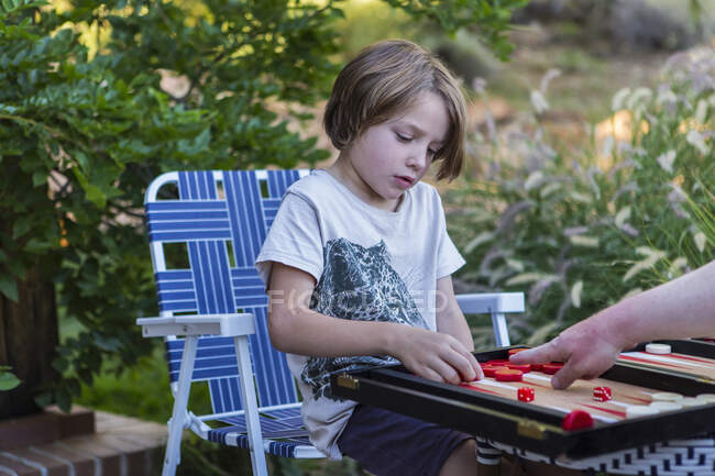 A young boy playing backgammon outdoors in a garden. — Stock Photo