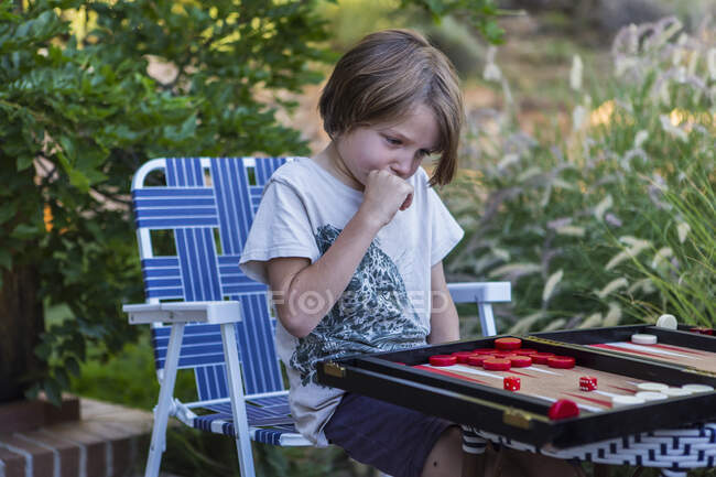 A young boy playing backgammon outdoors in a garden. — Stock Photo