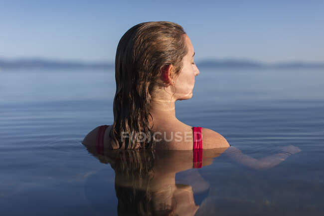 Menina adolescente, cabeça e ombros acima da água calma do lago ao amanhecer — Fotografia de Stock