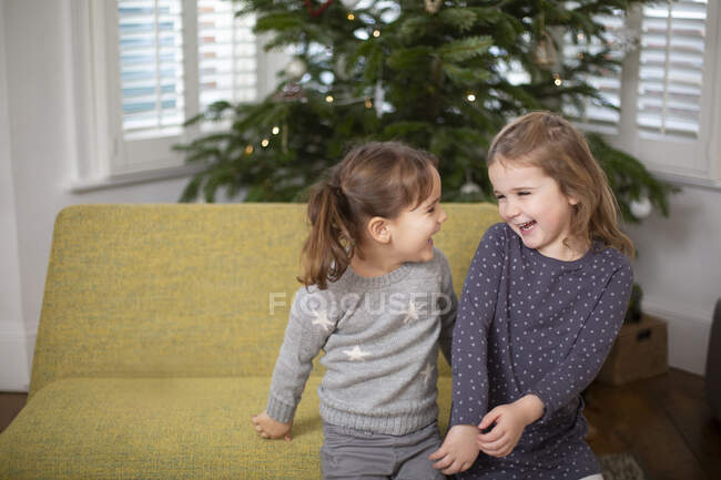 Дві молоді дівчата сидять на дивані у вітальні, посміхаючись один одному . — стокове фото