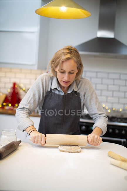 Mulher loira vestindo avental azul em pé na cozinha, assando biscoitos de Natal. — Fotografia de Stock