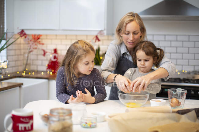 Mulher loira vestindo avental azul e duas meninas de pé na cozinha, assando biscoitos de Natal. — Fotografia de Stock