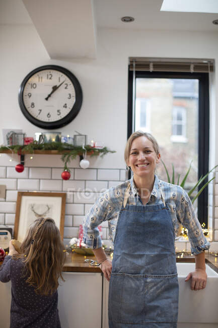 Donna bionda con grembiule blu in piedi in cucina, sorridente alla macchina fotografica. — Foto stock