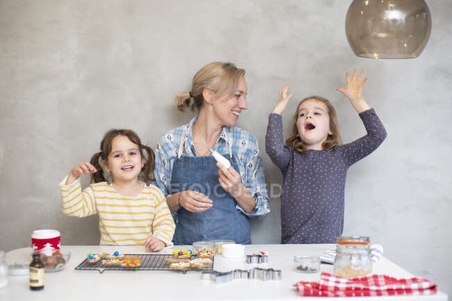 Donna bionda con grembiule blu e due ragazze che cuociono i biscotti di Natale. — Foto stock