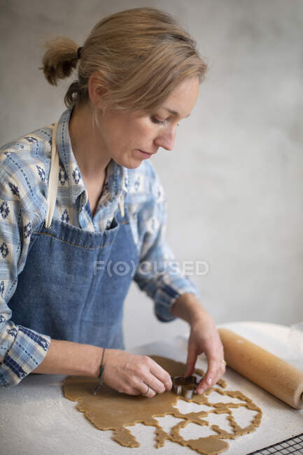 Mujer rubia vistiendo delantal azul cortando galletas de Navidad. - foto de stock