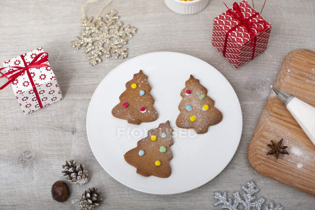 High angle close up of Christmas presents, decorations and Christmas Tree cookies on a white plate. — Stock Photo