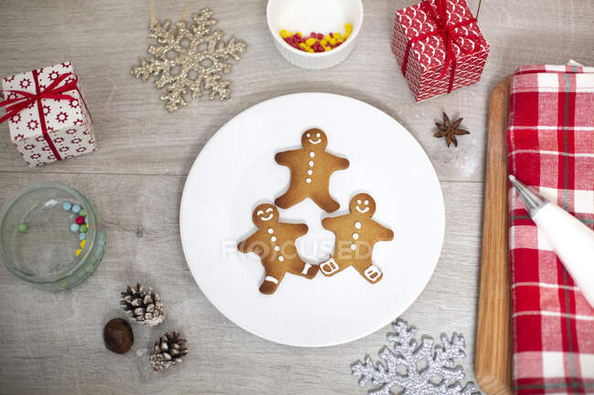 High angle close up of Christmas presents, decorations and Gingerbread Men on a white plate. — Stock Photo