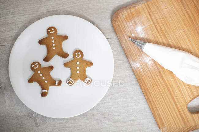 High angle close up of wooden cutting board and Gingerbread Men on a white plate. — Stock Photo