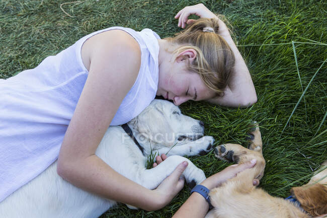 Duas meninas adolescentes deitadas no gramado, abraçando seus cães Golden Retriever. — Fotografia de Stock
