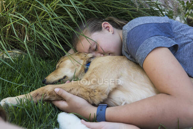 Teenage girl lying on lawn, hugging her Golden Retriever dog — Stock Photo