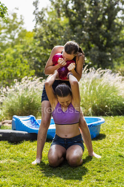 Two teenage girls wearing swimwear playing with water balloons in a garden. — Stock Photo