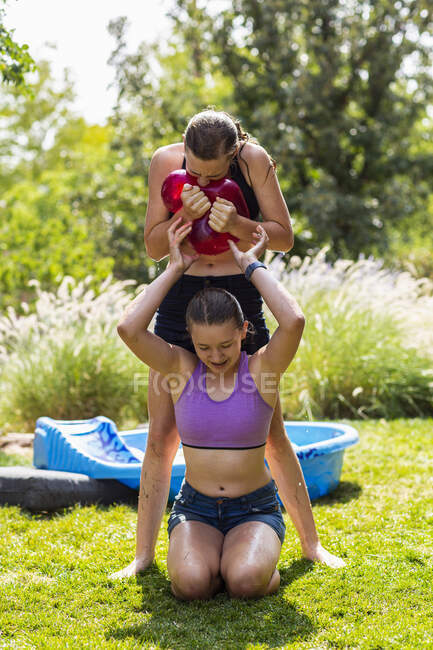 Две девочки в купальниках играют с водяными шариками в саду. — стоковое фото