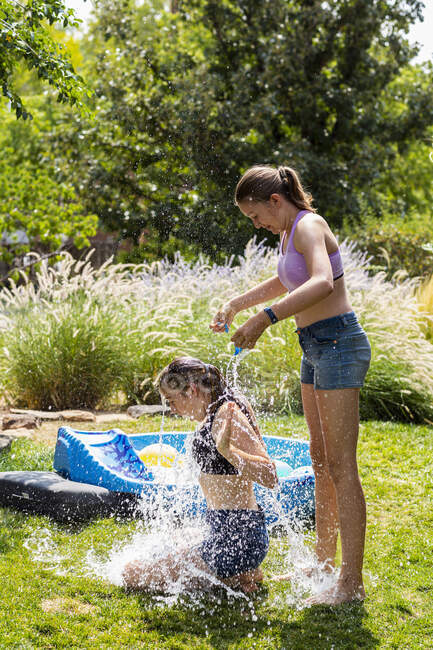 Две девочки в купальниках играют с водяными шариками в саду. — стоковое фото