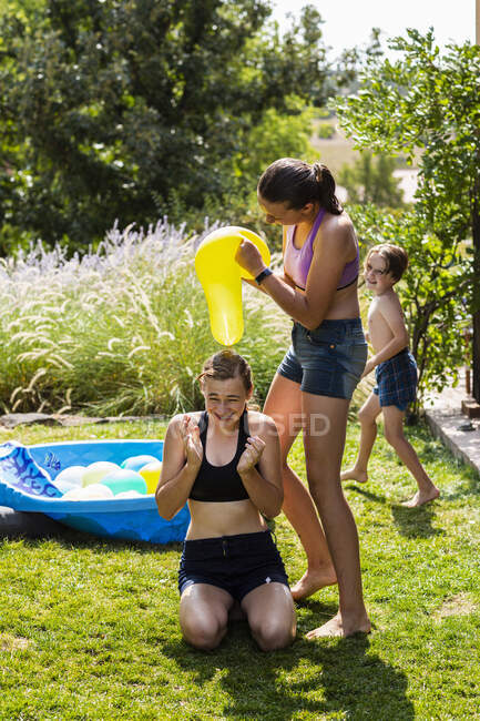 Due ragazze adolescenti che indossano costumi da bagno giocando con palloncini d'acqua in un giardino. — Foto stock