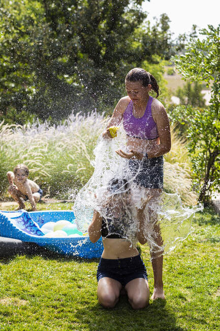 Zwei Teenager in Badebekleidung spielen mit Wasserballons in einem Garten. — Stockfoto