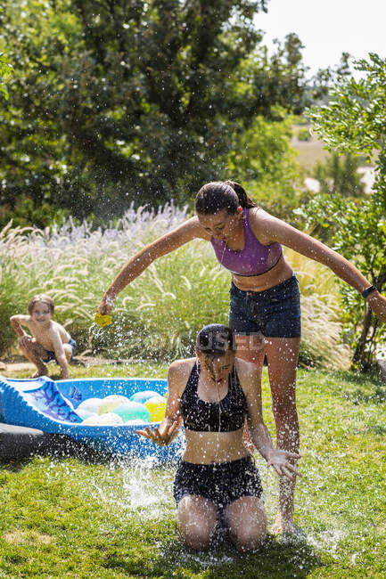 Zwei Teenager in Badebekleidung spielen mit Wasserballons in einem Garten. — Stockfoto