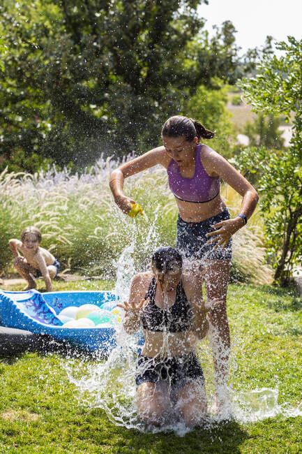 Dos adolescentes con traje de baño jugando con globos de agua en un jardín. - foto de stock